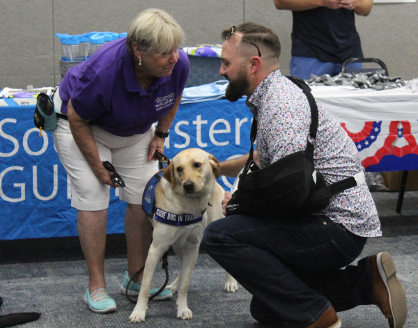 man crouching down to pet a dog while a woman crouches down to speak to him.