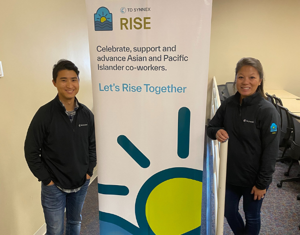 2 team members smiling next to a sign that says "Rise - Celebrate, support, an advance Asian and pacific Islander co-workers."