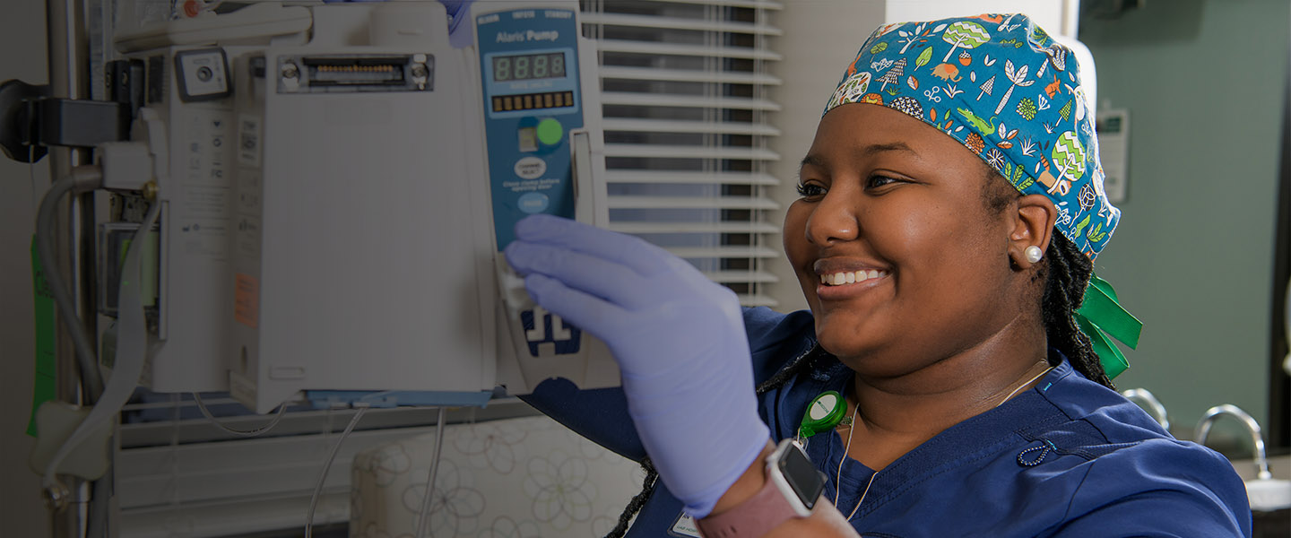Woman in scrub cap and gloves smiling and adjusting medical equipment