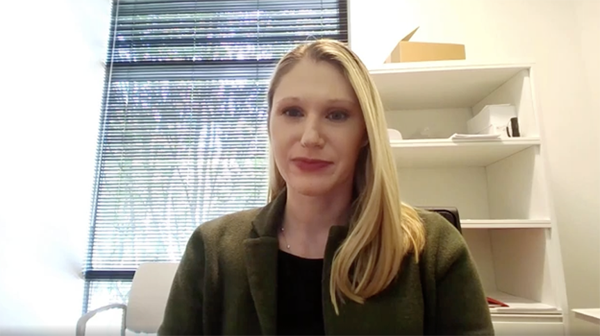 Person looks directly at camera with office window and bookshelves in background.
