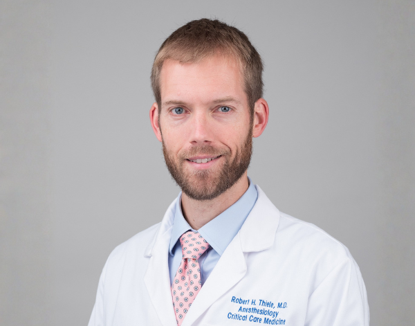 Physician looks directly at camera wearing white coat and a tie that is light pink and blue.