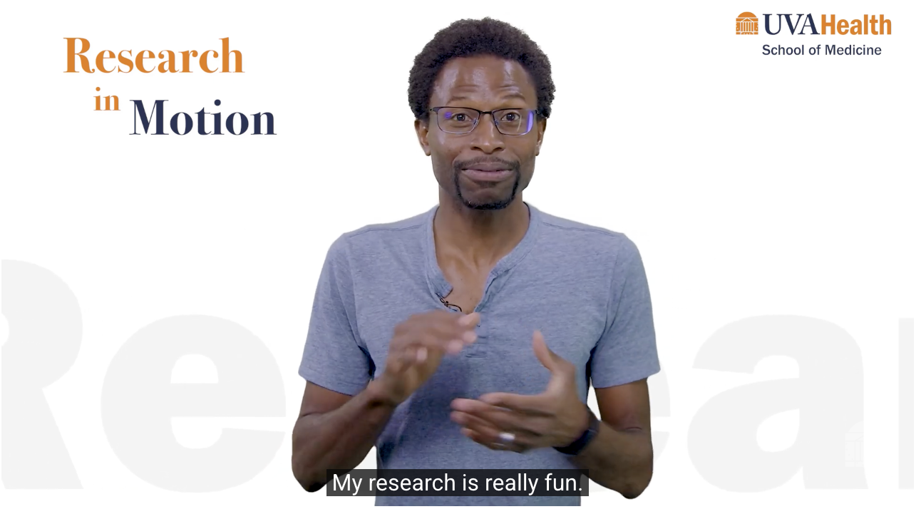 Person wearing a gray T-shirt gestures with both hands while speaking against a white background. On-screen text reads “Research in Motion,” with the UVA Health School of Medicine logo in the upper right.