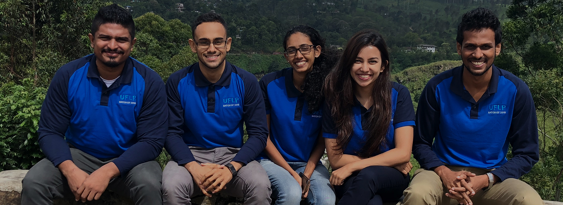 5 smiling people sitting in a row outside in UFLP branded shirts