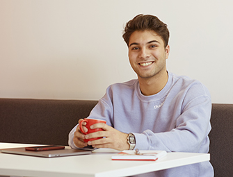 Kille sitter med en kaffekopp och ler mot kameran