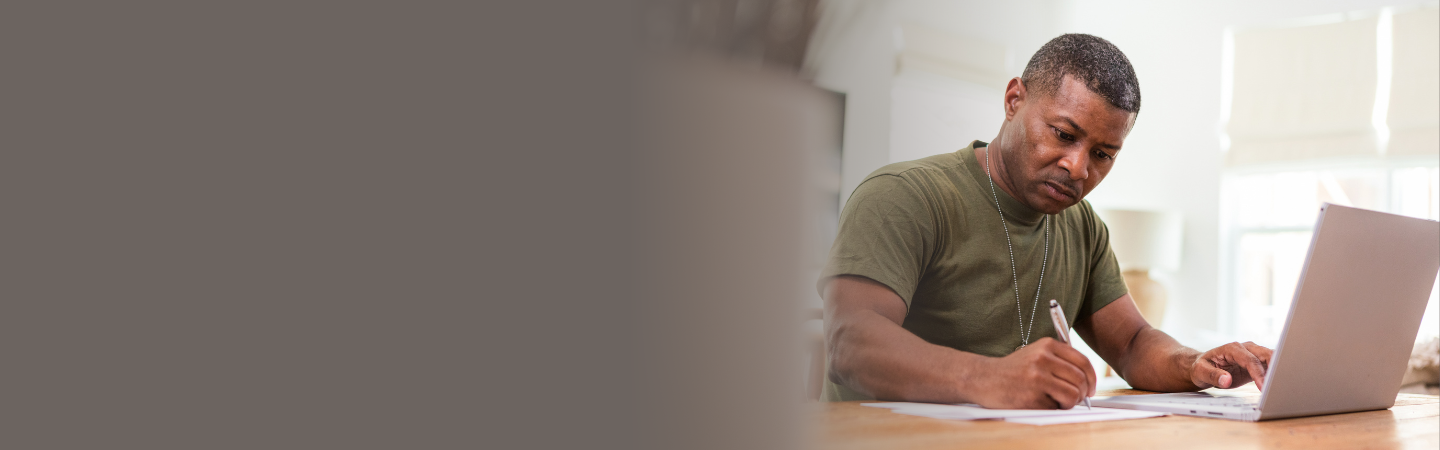 A military service member takes notes and works on a laptop.