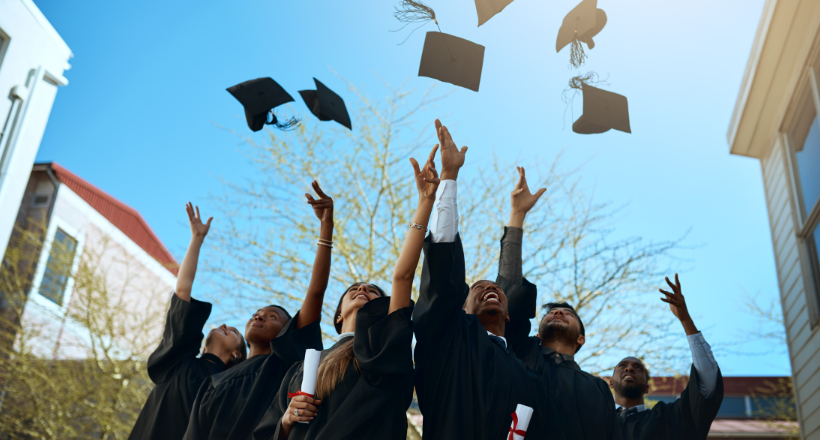 A group of six graduates through their caps in the air.