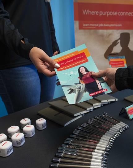 A recruiter hands an applicant a brochure to learn more about BAE Systems at a hiring event.