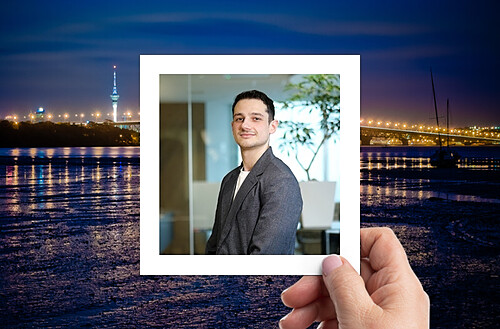 A hand holds a photo of four smiling people taking a selfie, with a vibrant city nightscape in the background.