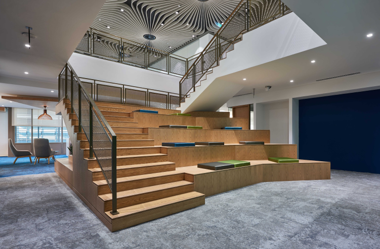  A wide staircase with built-in seating and green cushions, surrounded by open office spaces, showcasing modern architectural design.