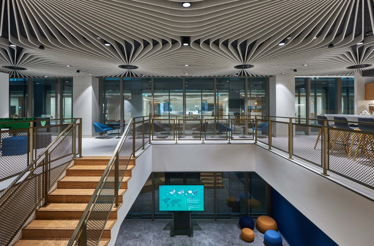 A view of the staircase with intricate ceiling details and open office seating, connecting the upper and lower levels of a workspace.