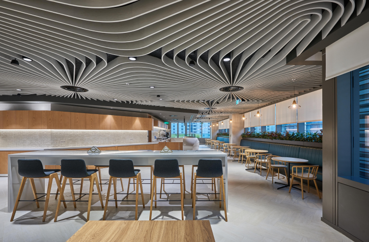  A cafeteria-style space with high-top seating and modern wooden finishes under a unique ceiling design.