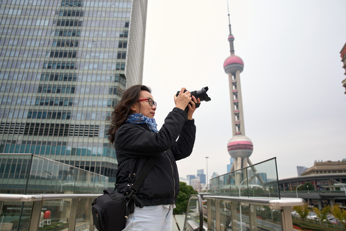 A hand holds a photo of four smiling people taking a selfie, with a vibrant city nightscape in the background.