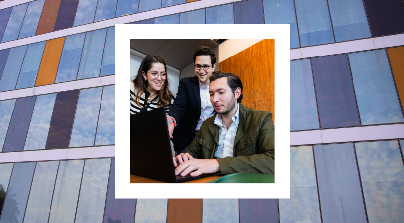 Three colleagues are gathered around a laptop, appearing engaged in a collaborative task. One woman and two men, one of whom is seated at the laptop, are all looking at the screen, suggesting a moment of shared focus. They are in an indoor setting, possibly an office. The image is superimposed onto a background of a modern building with a distinctive glass facade reflecting the sky.
