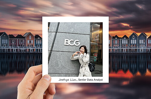 A hand holds a photo of a person in a headscarf with hot air balloons in the sky, against a backdrop of glass building reflections.