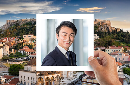 A hand holds a photo of four smiling people taking a selfie, with a vibrant city nightscape in the background.