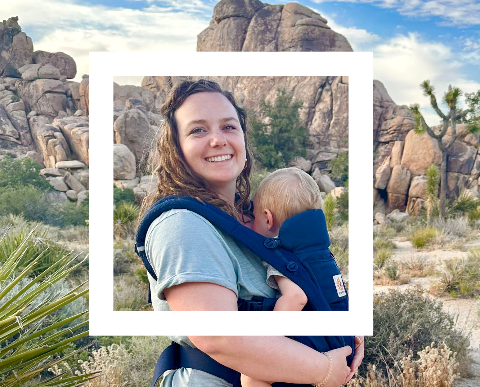 An adult carrying a child in a front-facing baby carrier, both facing away from the camera. They are outdoors with rocky desert terrain and sparse vegetation in the background. 