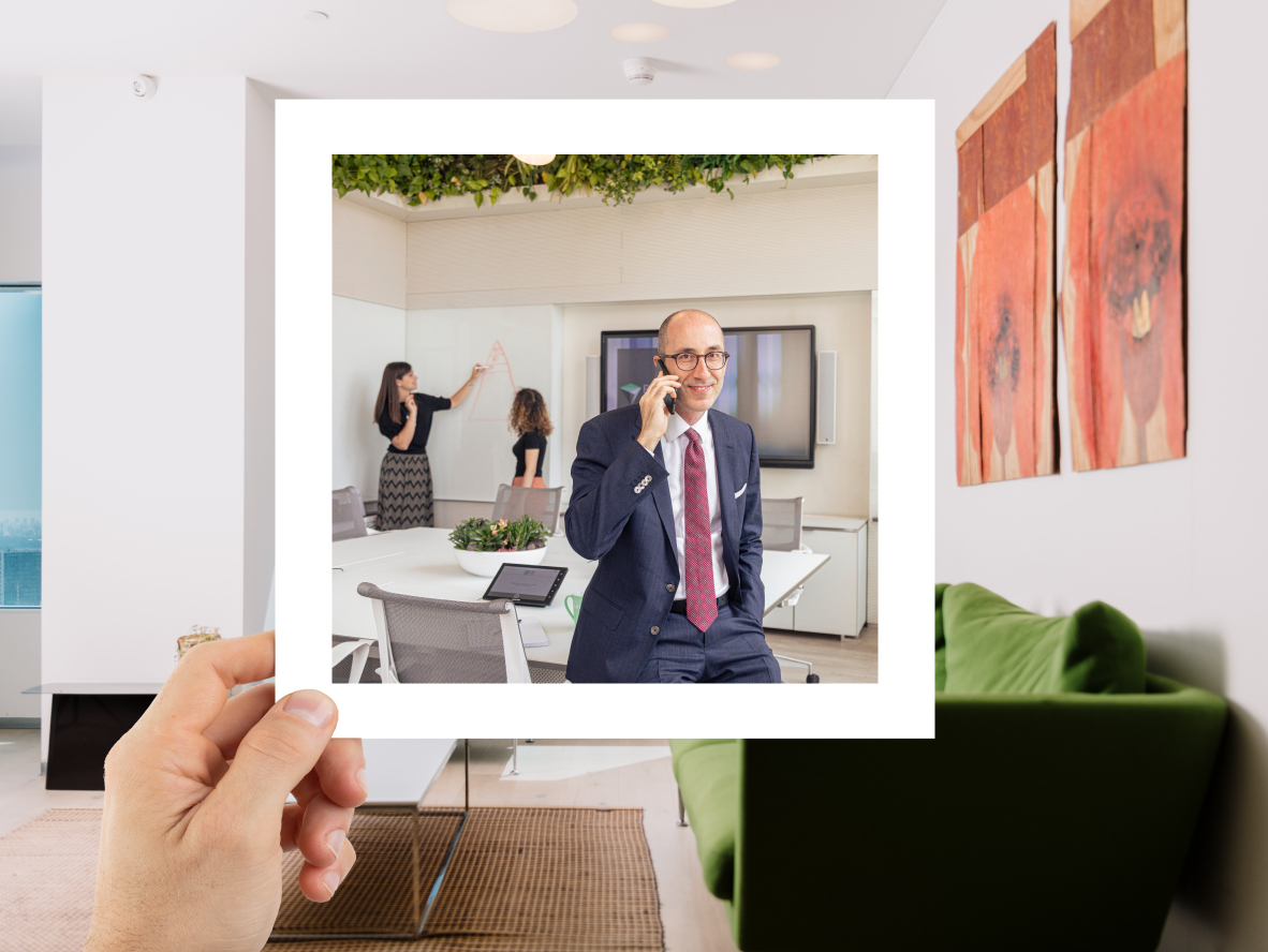 man on the phone in a suit in an office being held by a hand on a frame in another office