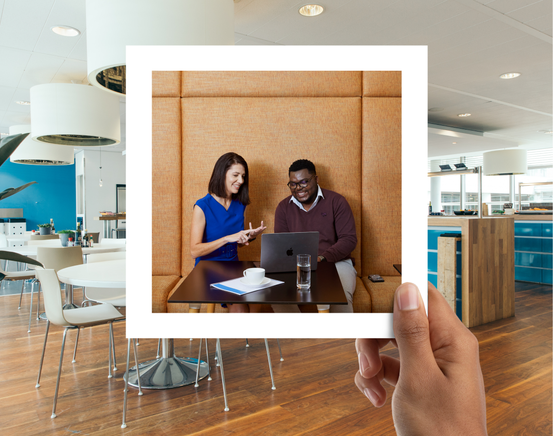 one man and woman working on a laptop in a photo frame held by a hand inside of a kitchen area