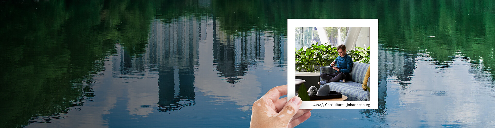 A panoramic banner image featuring a hand holding a photograph against a serene backdrop of a calm, reflective lake. Inside the photo, a man named Josef, identified as a consultant from Johannesburg, is seated comfortably in a modern lounge area surrounded by lush indoor plants. He is focused on a tablet, suggesting a moment of work or study. 