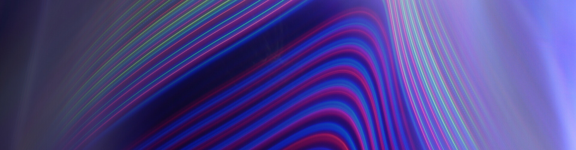 The image displays an abstract pattern with curved, multicolored lines. The lines predominantly feature shades of blue, purple, red, and green, creating a dynamic and flowing effect across a darker background. The overall aesthetic is modern and visually captivating, evoking a sense of motion and energy.