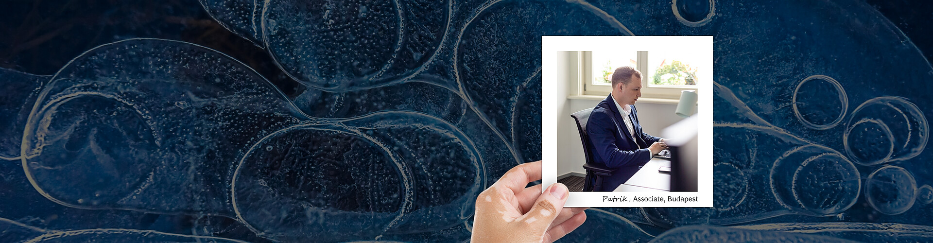 This panoramic banner image features a mesmerizing abstract background of deep blue ice patterns, possibly frozen bubbles in a pond or lake. Overlaying this is a smaller portrait of a man named Patrik, identified as an Associate in Budapest. In the portrait, Patrik is seen from the side, focused on his work at a laptop in a bright, modern office setting. His attire is professional, consisting of a blue blazer and a white shirt. 