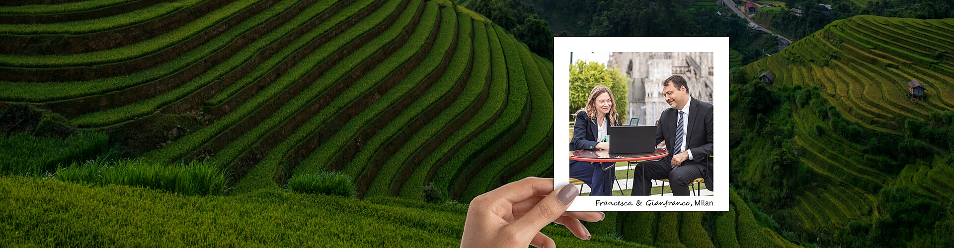 This panoramic banner image showcases a vivid and detailed view of lush green rice terraces, presenting an impressive example of landscape architecture and sustainable farming. Overlaying this serene background is a photograph held by a hand, featuring Francesca and Gianfranco in an outdoor business setting in Milan, engaged in a discussion over a laptop.