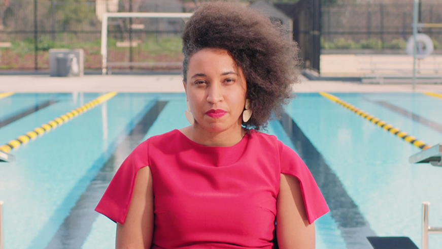 A play button icon for a video. The thumbnail of the video is of an individual sitting in front of a swimming pool with lane dividers. The person is wearing a red top, and the background includes starting blocks and pool lanes, suggesting a competitive swimming environment