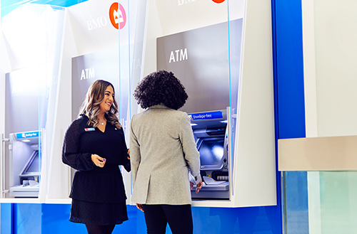 Female employee smiling to another female in front of ATM
