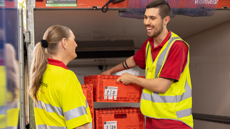 Two Coles Customer Service Agents unloading groceries from a van