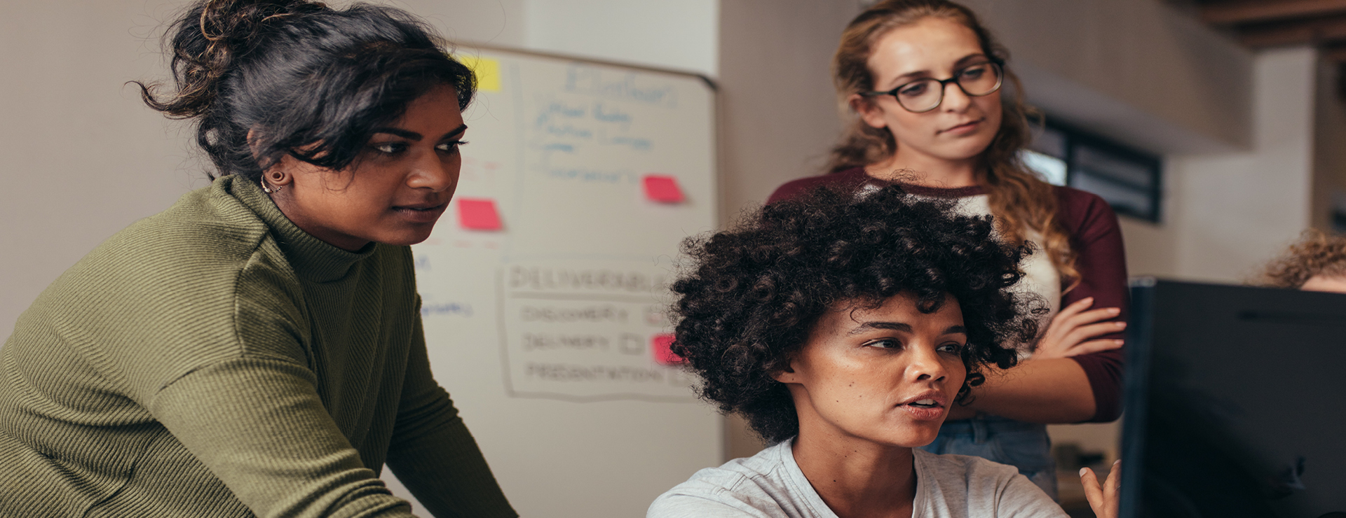 Three women in a meeting look at a computer