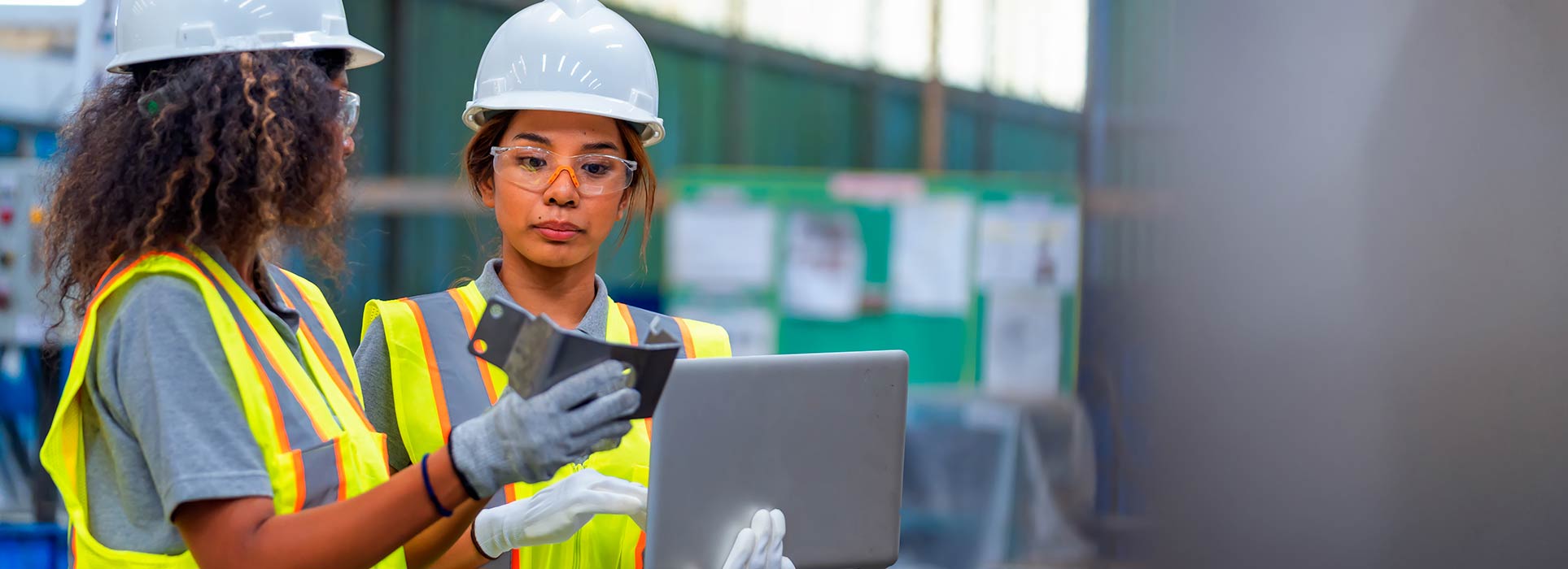 Two female manufacturing workers in personal protective equipment, looking at metal