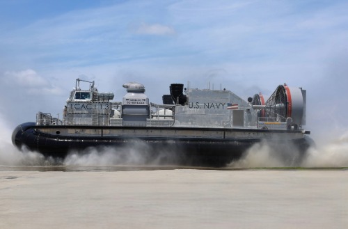 U.S. Navy air cushion landing craft from Textron Systems traveling at high speed over shoreline terrain.