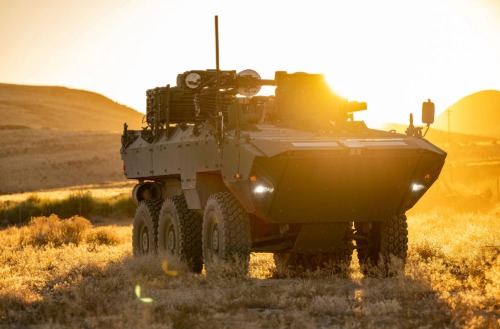 Textron Systems armored military vehicle driving through desert terrain during field operations at sunset.