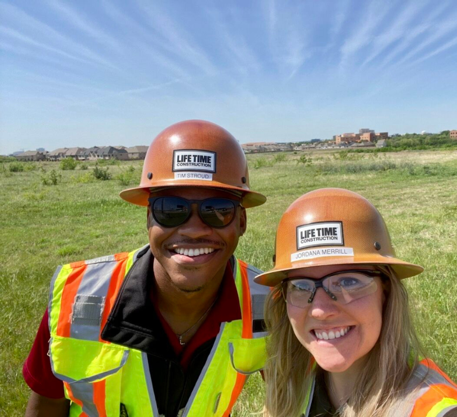 Two Life Time team members smiling with Life Time construction hats on.