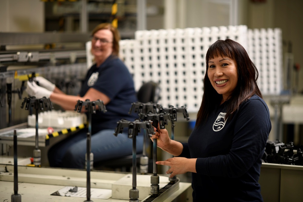 Two Philips employees in a manufacturing factory smiling at the camera