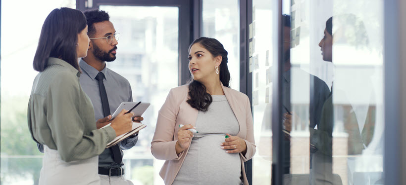 Two women, one pregnant, and a man standing in a semi-circle talking. 