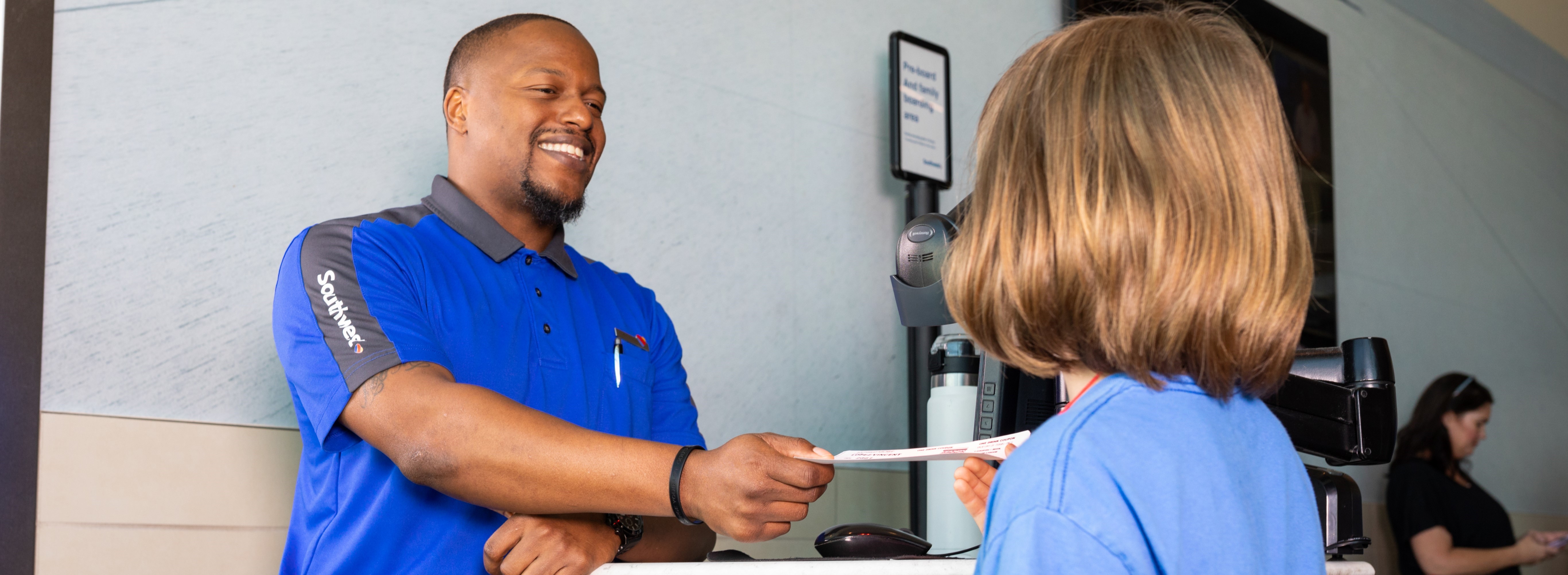 Operations Agent smiling handing passenger a boarding pass.