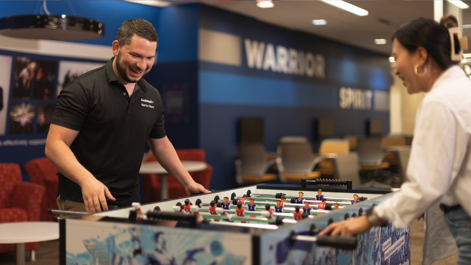 Two employees smiling and playing foosball