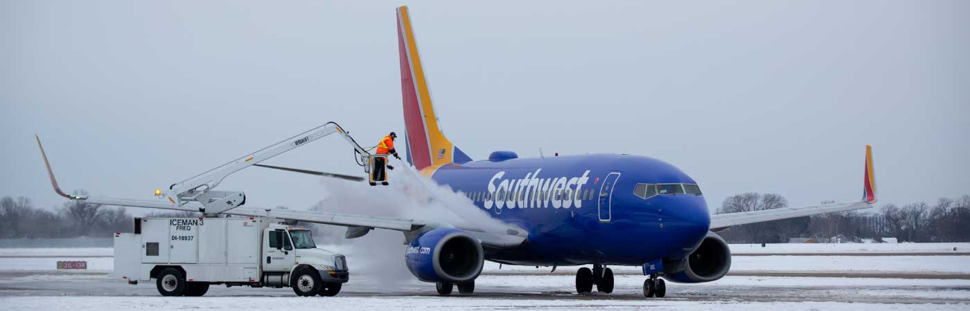Wide shot of ramp agents deicing a Southwest airplane in the snow from a crane.