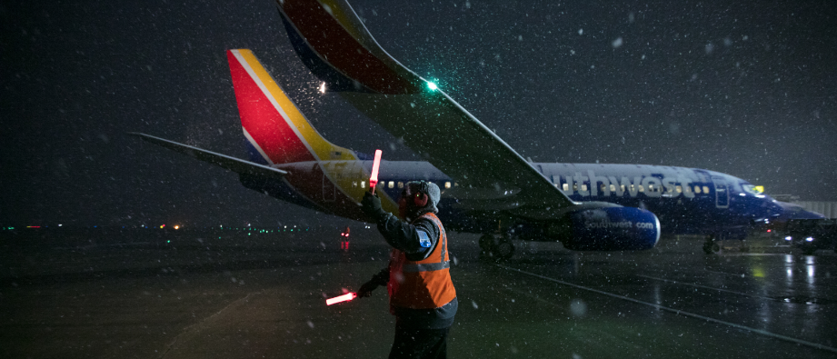 A Southwest Ramp Agent marshalling in an aircraft at night in snow, cold weather