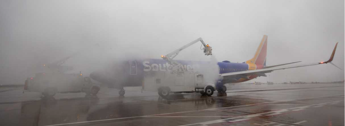 Wide shot of ramp agents deicing a Southwest airplane in the snow from a crane.
