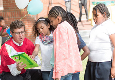 Man opens children's book for a group of children and little girl points to a picture
