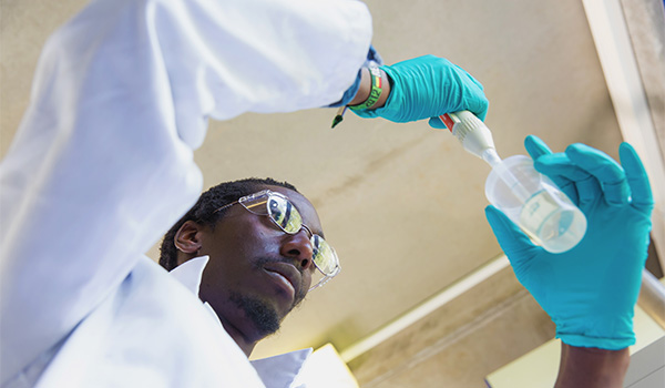 UCB Colleague in safety glasses and white lab coat using a pipette