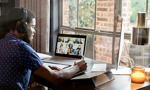 Young man with headphones, owrking on a laptop while taking a class online