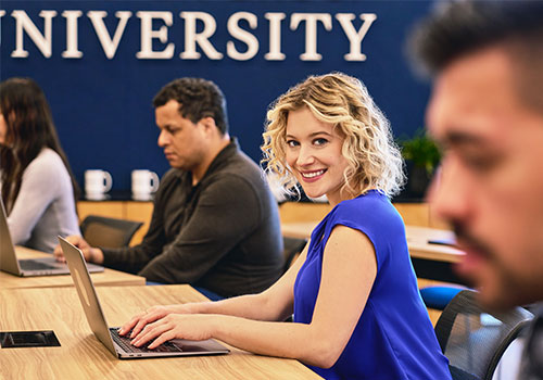 Blonde woman, smiling at the viewer and working on a laptop