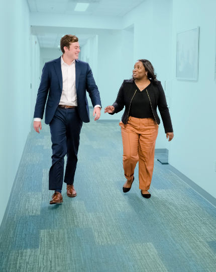 Chris and Ronda walk down a hallway as they have a discussion.