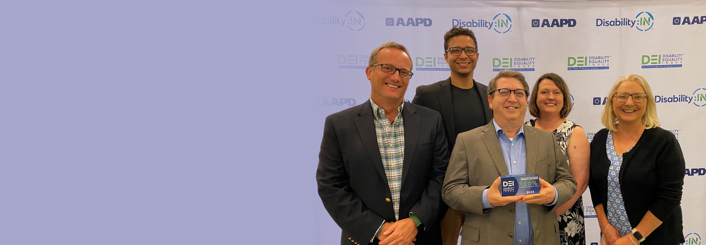 Five BAE Systems posing with an a crystal trophy at the Disability: IN global conference after earning 100% on the disability equality index.