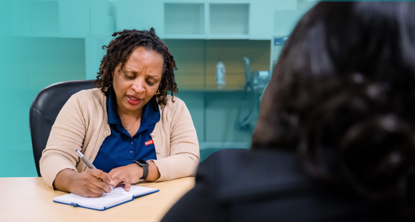 A BAE Systems employee writes notes in a notebook as she speaks to a colleague. 