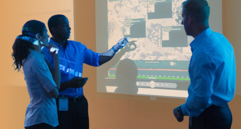 Three intelligence analyst gather around a screen to discuss imagery