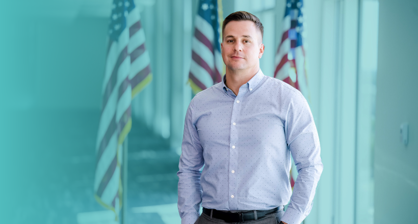 Tony, a program manager, stands for a photo in front of three American flags.